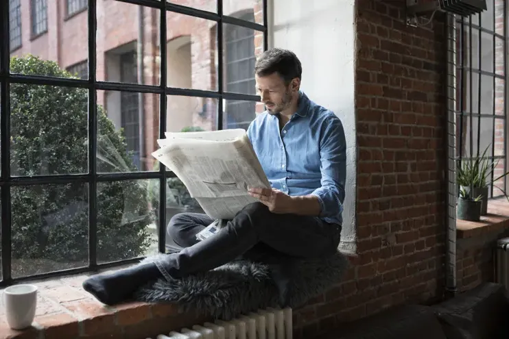 Man sat on window ledge reading newspaper
