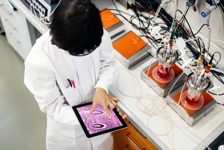 一位亚洲女科学家正在实验室做研究. 她在桌子旁边的平板电脑上工作，桌子上放着装满物质和其他科学设备的烧瓶.